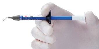 Hand holding 3M flowable composite syringe.
