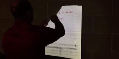 A technician demonstrates how to install a reflective graphic film wrap on a textured wall.
