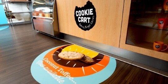 A restaurant has a “Cookie Cart” wrap logo on the counter and a colorful graphic wrap on the floor.
