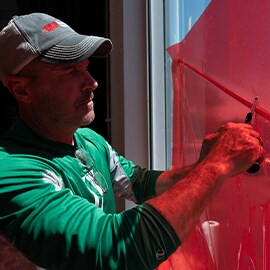 A graphic installer with a 3M baseball cap installs red window film.