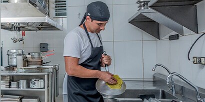 A restaurant worker scrubs a pan in a commercial kitchen.

