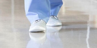 Person in disposable paper pants and booties walking toward the camera over a clean floor
