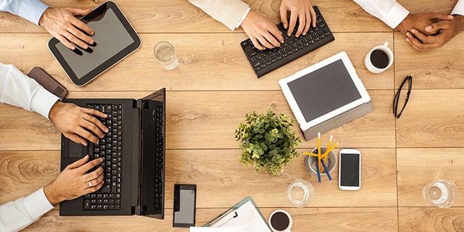 Four people meeting at a table while looking at laptops and tablets 
