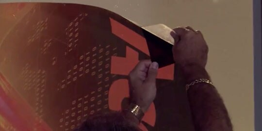 A pair of hands installs a perforated window film.
