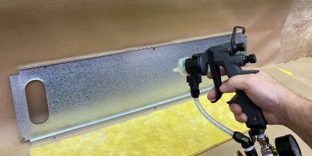 A worker sprays the inside of a metal panel before attaching insulation
