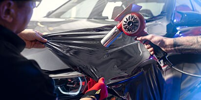 Installer pulls Gloss Black 3M Wrap Film Series 2080 over a car hood 
