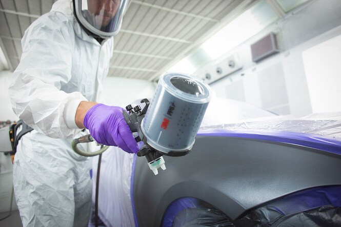 person using automotive paint spray gun in a collision repair setting
