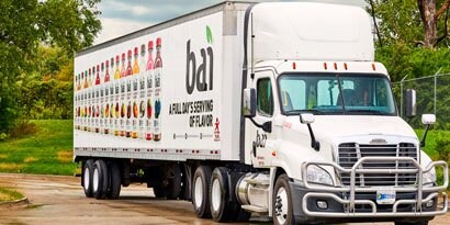 A semi-truck features crisp images of beverage bottles and a logo on its vehicle wrap.
