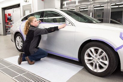 Technician masking large panels on a car in a body shop.
