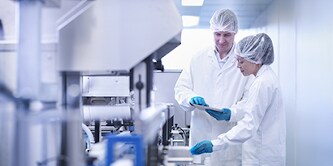Image of factory workers in a brightly lit environment, using a mobile device.

