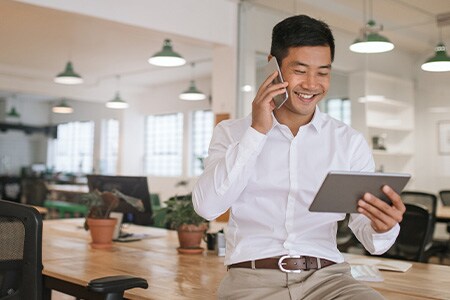 Image of smiling businessman talking on phone and looking at tablet.
