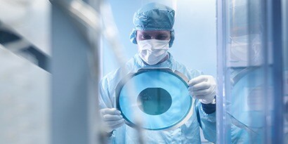 Man in scrubs holding clear blue disc from semiconductor process protection.
