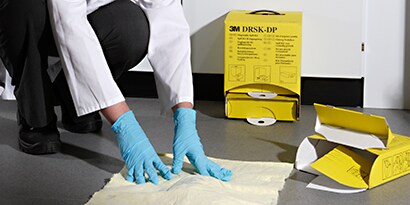 lab worker cleaning up a floor chemical spill with a spill kit.
