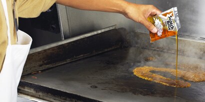 3M Scotch-Brite Quick Clean Griddle Liquid being poured onto a hot griddle
