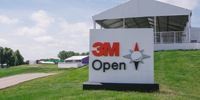 A large, square 3M Open sign is on a hill in front of an open-air building.
