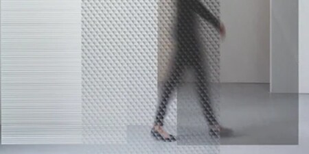 An office worker walks behind glass surfaces with 3M glass finishes whose attractive patterns create privacy.
