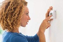 woman checking the temperature on her smart thermostat