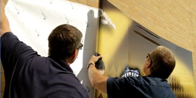 Two men put up a white 3M controltac print film on a wall
