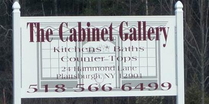 A sign wrapped in 3M colored films that says The Cabinet Gallery and phone number in maroon font.

