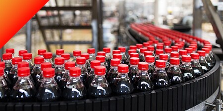 Hundreds of plastic bottles of dark soft drinks on a conveyer belt.
