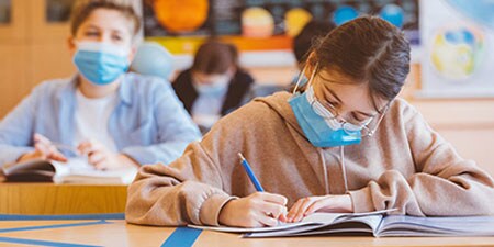 Children with masks on working on homework on a desk cleaned with 3M Instant Microbe Removing Wipes.
