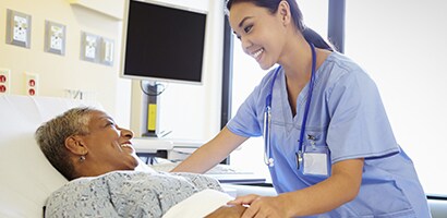 A clinician holding the hand of an elderly patient in a hospital setting.
