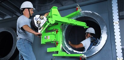 Worker operating horizontal confined space entry device at opening in side of large tank
