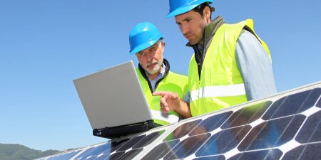 workers looking at laptop on top of solar panels
