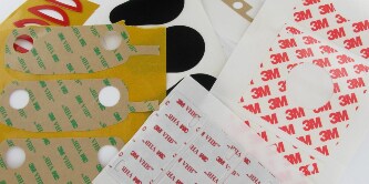 Image of various 3M™ VHB™ Tape sheets, some with die-cuts removed
