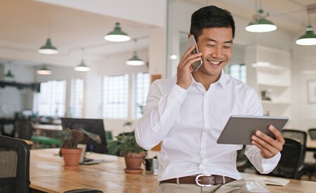Image of smiling businessman talking on phone and looking at tablet.
