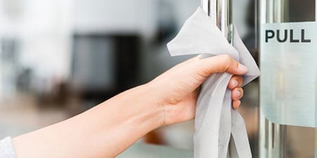 A person wiping a stainless steel fridge handle with 3M's Instant Microbe Removing Wipes.
