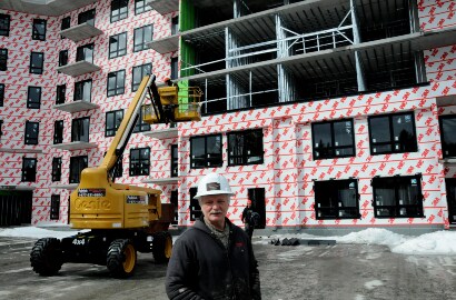 Image of a man standing on a job site with snow and a building partly wrapped with a 3M air barrier
