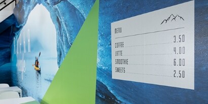 A print wrap film lists drink prices and has an image of kayakers and a green triangle.
