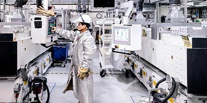 Manufacturing facility worker with protective gear, adjusting settings on machine
