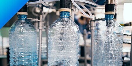 Three plastic bottles being filled with water in a production facility.
