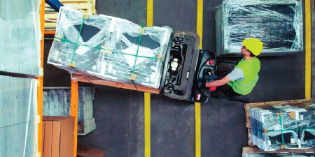 Forklift operator maneuvering a pallet across taped lane marks into a storage area
