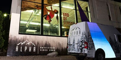 A graphic wrap on a van reflects blue and white light at night.

