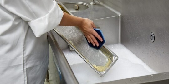 A commercial kitchen worker uses the Scotch-Brite™ Quick Clean Griddle Cleaning System to clean a griddle.
