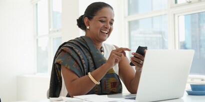 Woman smiling while using cellphone and laptop