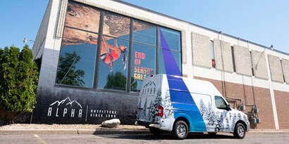 A truck with a vehicle wrap is in front of a building with a large window wrap.
