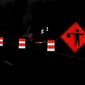 Utility truck with traffic cones is parked in road work zone with highly visible traffic drums and flagger-ahead sign