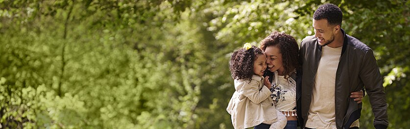 young family on a walk with green trees in the background
