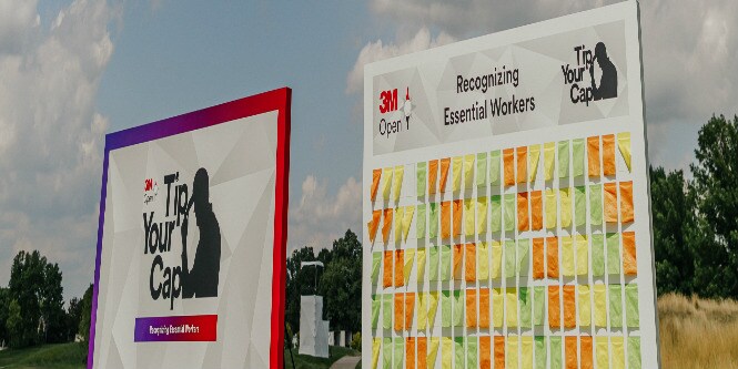 A shot of two large colorful outdoor display boards sitting on grass under a partly cloudy sky.
