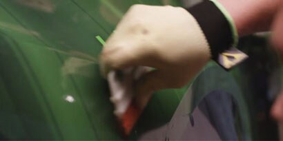 The hand of a graphic installer, wearing a latex glove, touches a green wrap.
