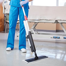 A nurse using a mop to clean the floor beside a hospital bed.