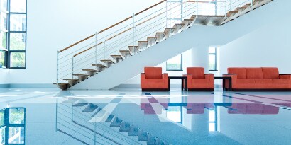 Lobby with clean, shiny floors, red chairs and couch, and long, modern staircase.
