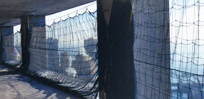 Image of vertical nets blocking open exterior walls of tall building under construction

