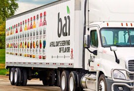 A semi-truck has a vehicle wrap with images of numerous colorful bottles.