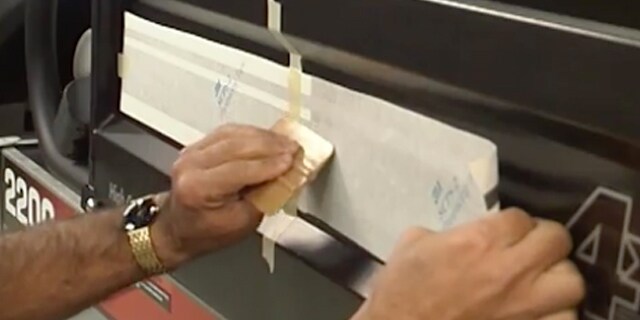 Man applying 3M film adhesive wrap to back of black car with a flat applicator
