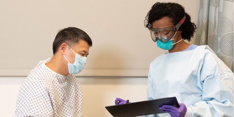 health care worker in a protective respirator and goggles conversing with patient(U.S.,English)

